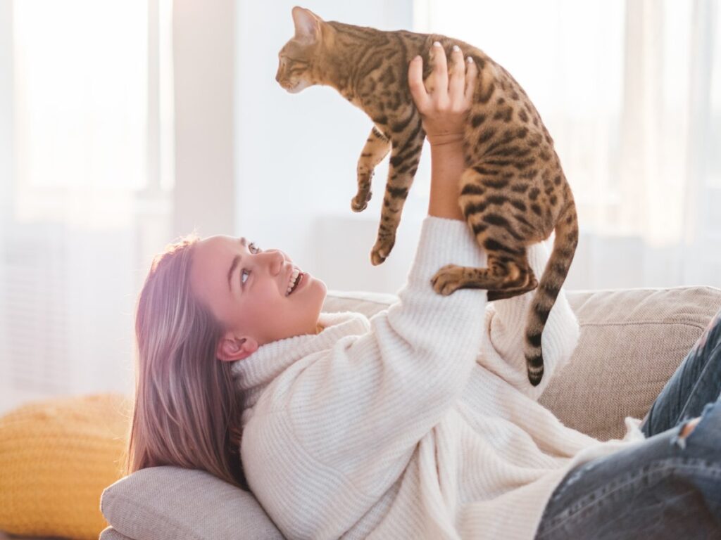 A girl is holding her cat high in the air