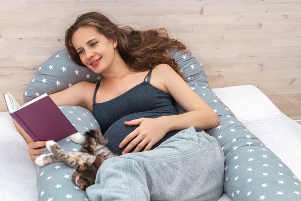 A pregnant woman is reading a book with her cat