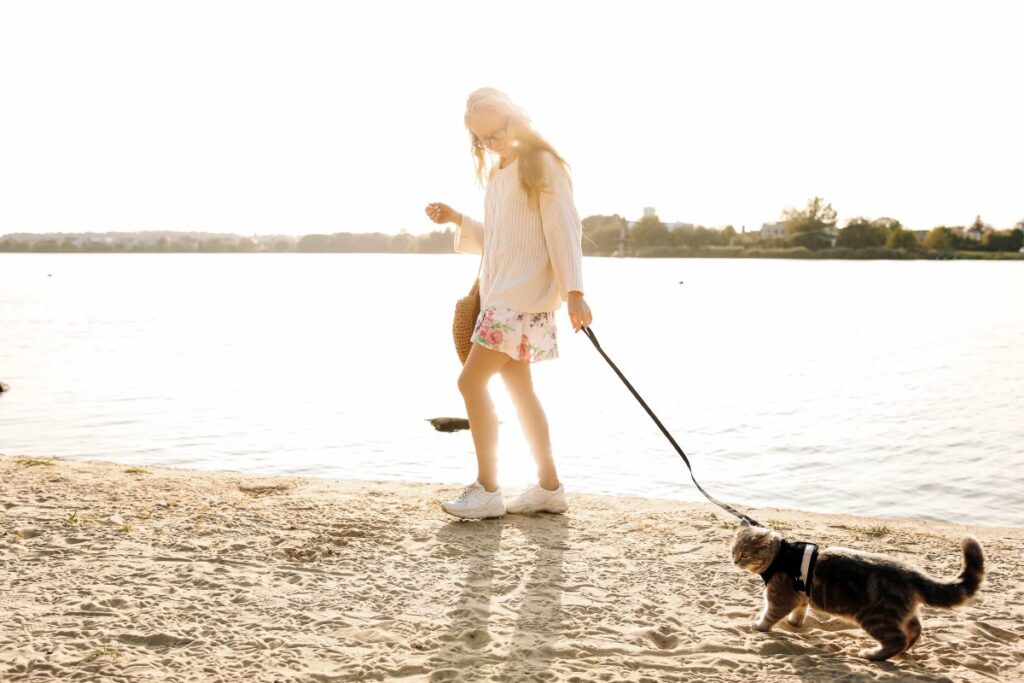 A woman is walking with her cat at the beach